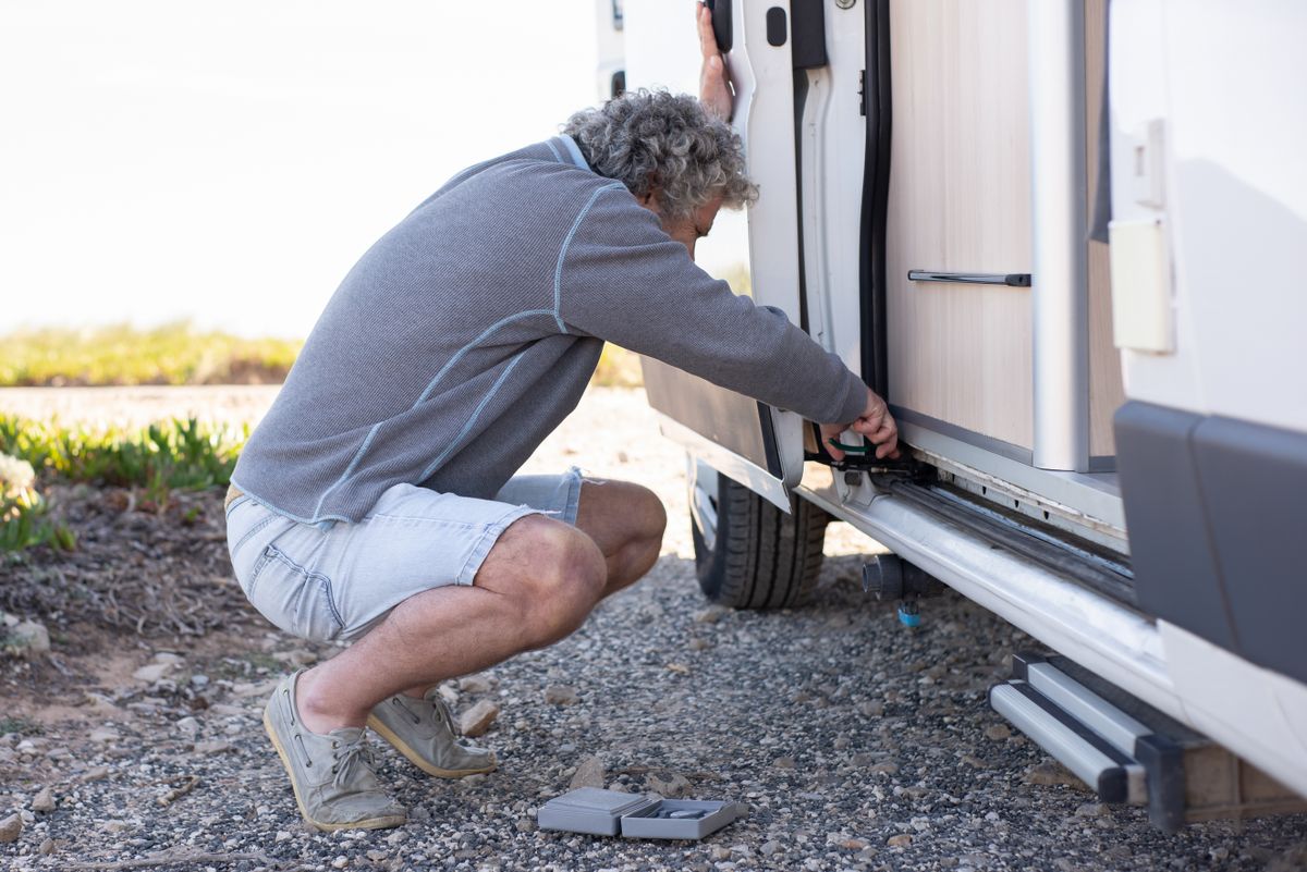 Man kneeling beside a camper van working at the entry step and lower sill area