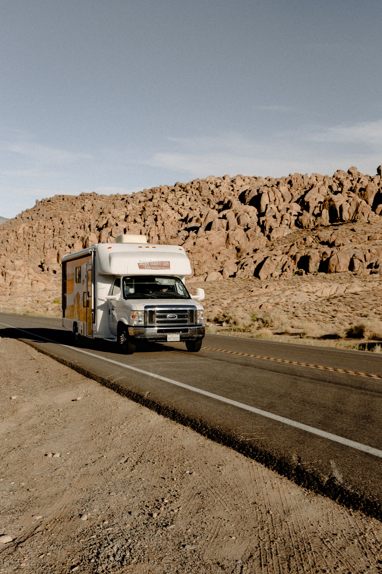 Motorhome on a sunlit desert highway with rocky terrain in the background