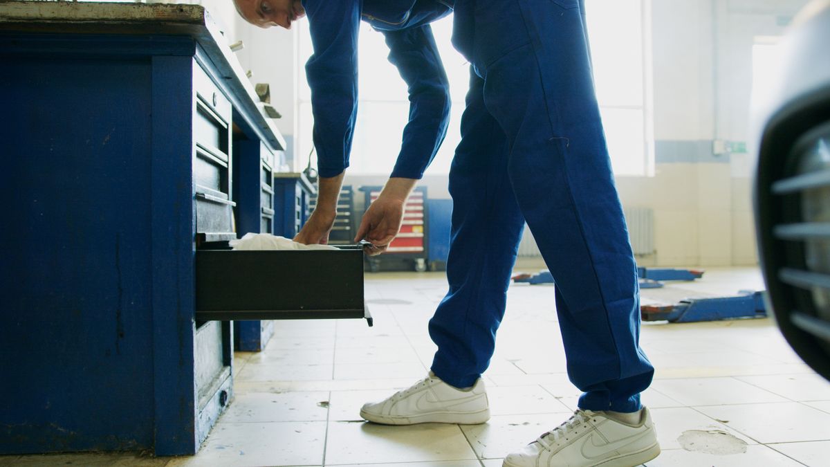 Technician in blue coveralls reaching into an open tool chest drawer in a workshop